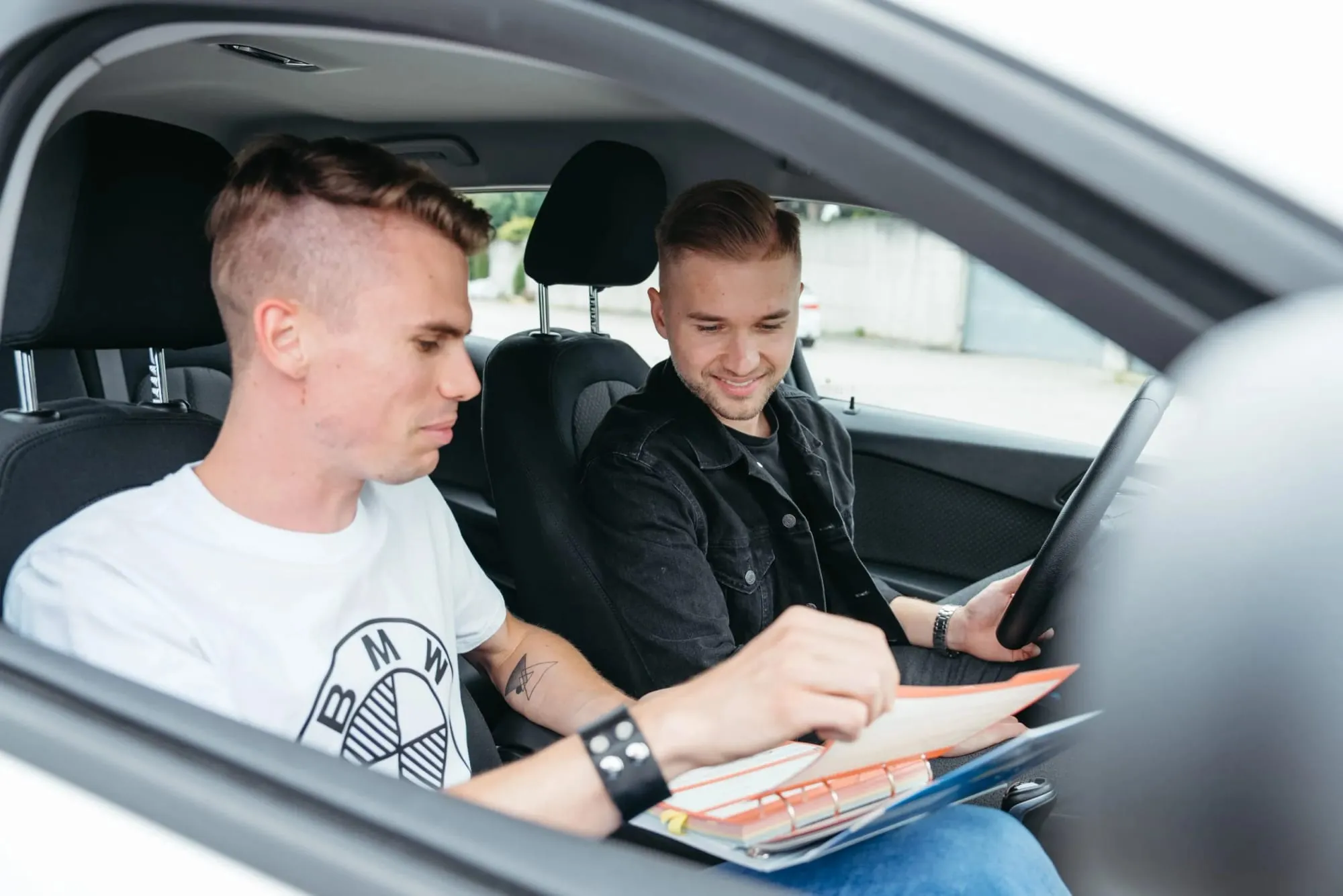 Ein Fahrlehrer bespricht mit einem Fahrschüler im Auto die Unterlagen